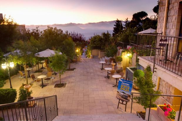 מתחם חוץ רומנטי מואר בערב בתאורה נעימה עם שולחנות ישיבה ושמשיות - Villa Galilee